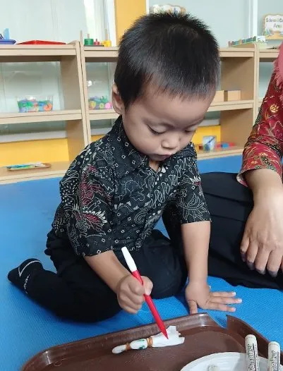 Seorang anak mewarnai kain untuk kegiatan batik